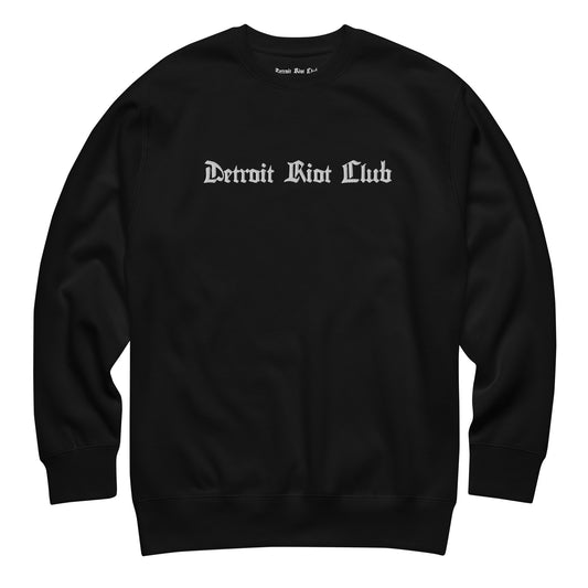 "Front flat lay of the 8.5oz heavyweight crewneck in void black with natural texture, highlighting the central embroidered gothic brand name logo."